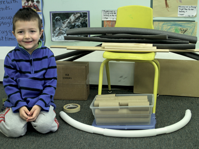 A student kneels on the floor in front of the materials for making a giant marble run.