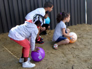 Students in a sandy playground, prepare to roll large plastic balls.