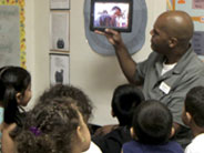 A teacher holds up an iPad to show a class of students a video.