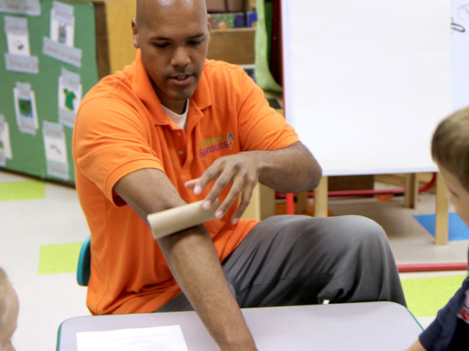 Teacher shows how he can use his arm as a ramp to roll a cardboard tube down.