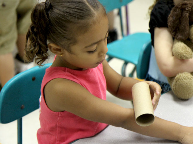 A student uses her arm as a ramp to roll a cardboard tube down.