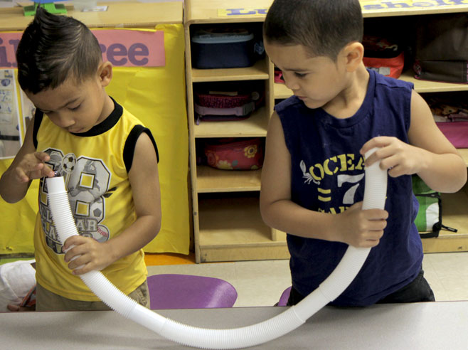 Students hold each end of a plastic tube. One student is putting a marble into one end of the tube.