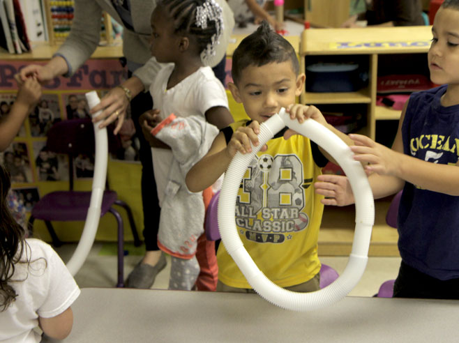 Two students play with a plastic tube. One is forming a circle out of the tube.