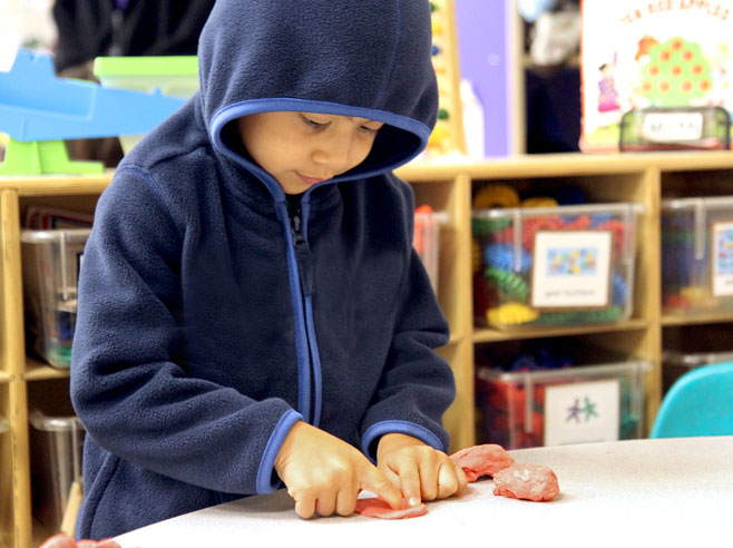 A student plays with red play-dough at a table.
