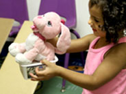 A student holds up a pink stuffed dog that she has placed in a plastic tub.