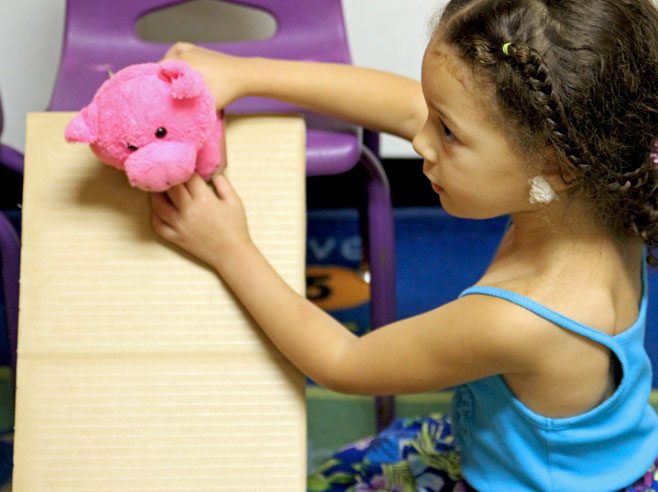 A student prepares to release a pink stuffed pig down a cardboard ramp.