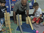 Students and a teacher kneel behind three different ramp set ups. 2 different sized balls are on the floor at the bottom of one of the ramps.