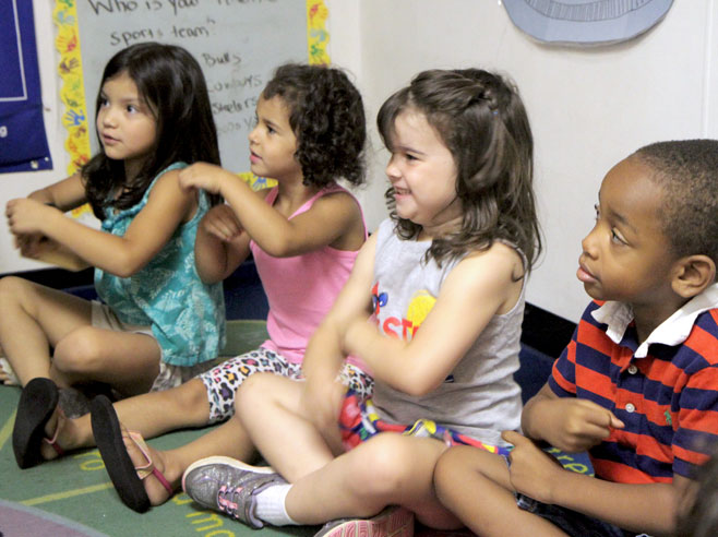 Four seated students make rolling motions with their arms.