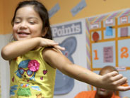 A student smiles as she demonstrates a sliding motion using her fingers on her own arm.