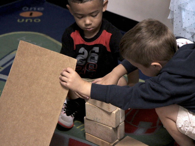 Two students work to build a ramp with wooden blocks and a piece of cardboard.