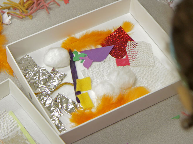 A cardboard box lid filled with a collage of materials of different textures and colors.