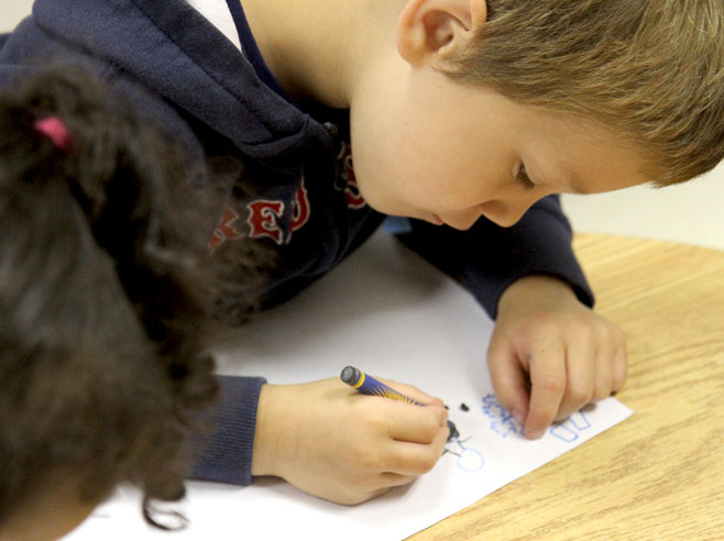 A student leans over a drawing he is making with crayon.