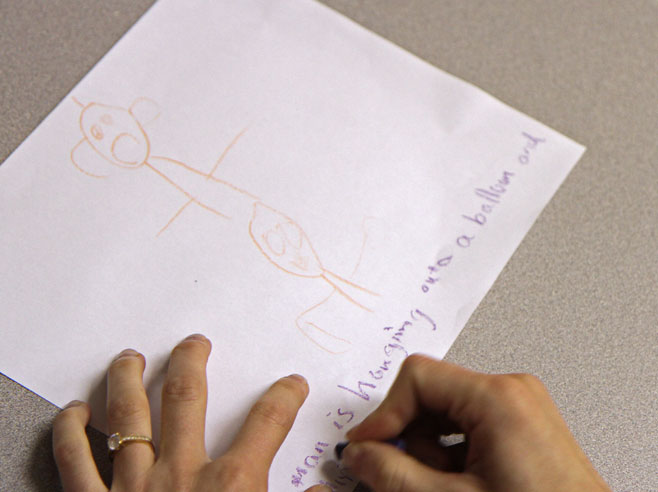 A teacher's hand can be seen captioning a drawing made by a student.