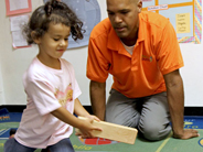 A student holds a wooden block as a teacher looks on.