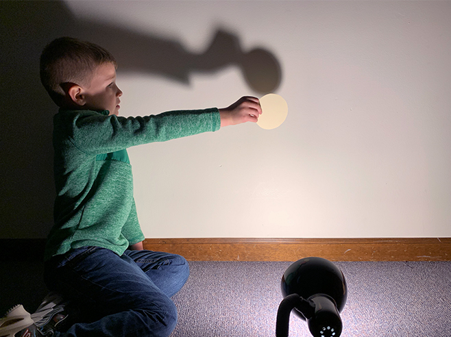 Light shining on student holding a circle to make a shadow on the wall.