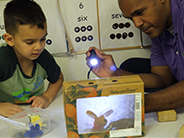 Teacher and student shining flashlight at a shadow box theater.