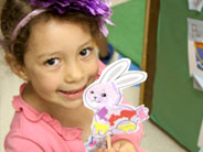 A student smiles for the camera, as she holds up her hand-collaged rabbit shadow puppet.