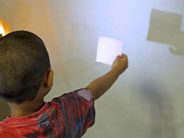 A student holds a square piece of paper in front of a white wall, creating a square shadow on the wall.