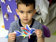 A student holds up his art work: a 2-D cut-out of a bird, brightly colored with markers.