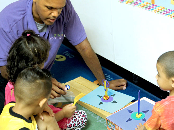 A teacher and three students are seated on the floor looking at two rotation maps, one with a pair of scissors and one with a ruler, both standing upright in Play-Doh.