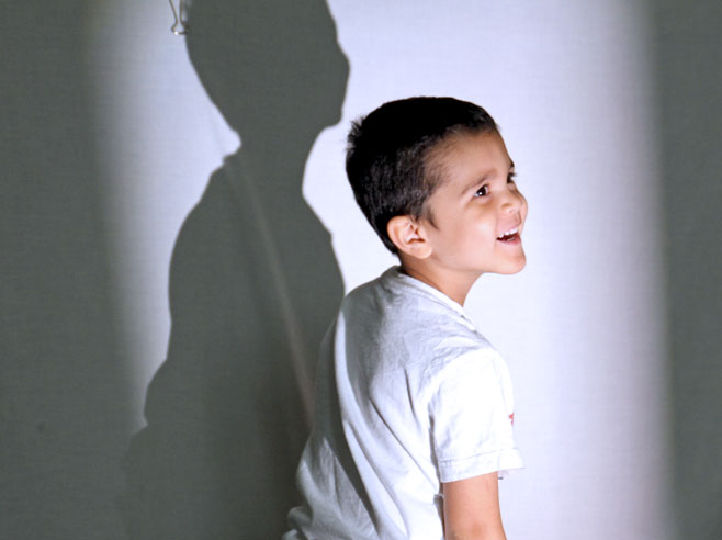 A student turns around smiling. His shadow is visible on the wall behind him.