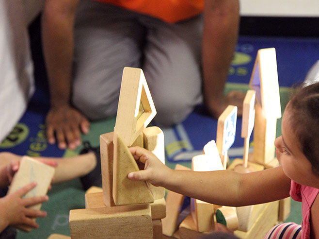 Students are building a structure on the floor, using wooden blocks of different shapes.