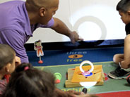 A roll of masking tape, stabilized in Play-Doh, stands in the middle of a rotation mat placed on the floor. A teacher points to a shadow created on the wall.