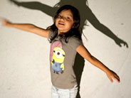 A girl with her arms outstretched stands against a backlit wall. Her shadow is visible.